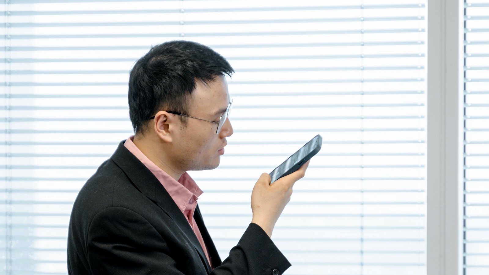 A man in an office speaks into a smartphone held in front of him.