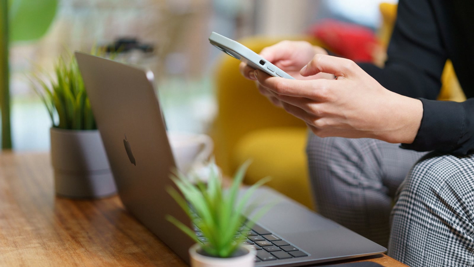 A person checks a smartphone beside an open laptop in a home setting.