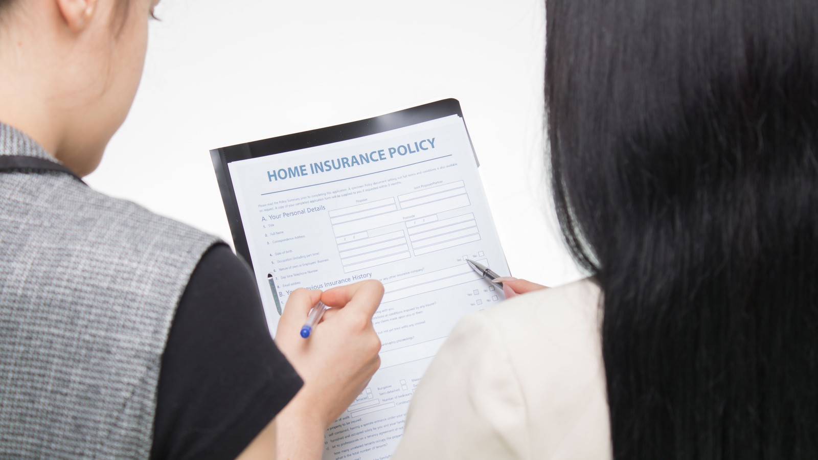 Two people sit at a table examining a printed home insurance policy form.