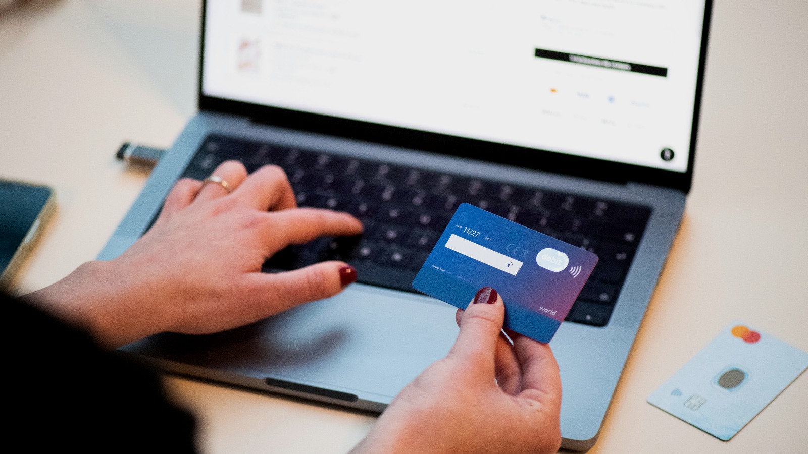 A person holds a bank card while entering information on a laptop during an online purchase.