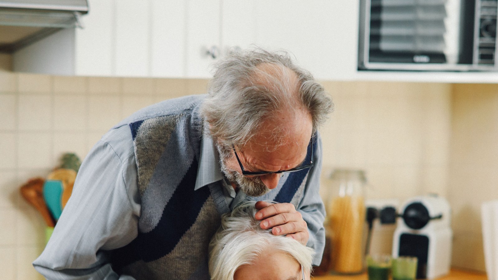 An older couple sits at a kitchen table reading a printed document together.