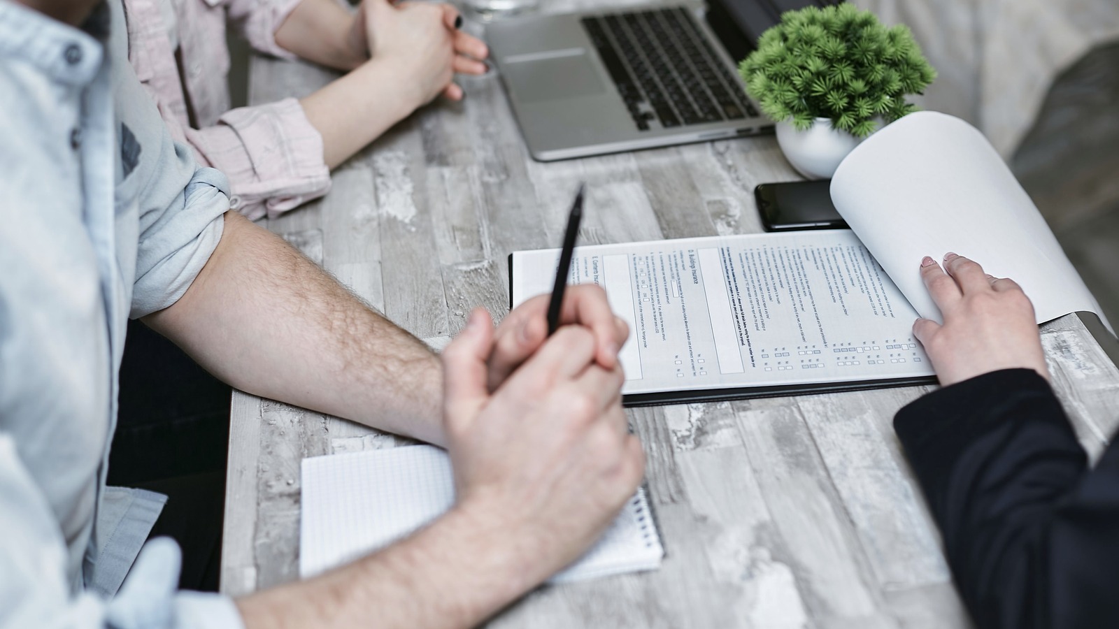 People review printed forms beside a laptop at a meeting table.